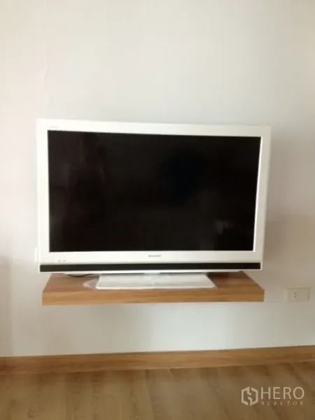 Condominium for rent in Khlong Toei, Bangkok - Flat-screen TV on a floating wooden shelf in a modern condo living area with wood floors.