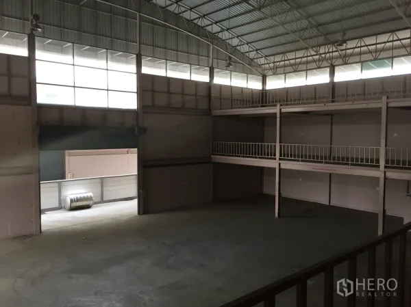 Factory for rent in Lam Luk Ka, Pathum Thani - High-clearance warehouse interior featuring mezzanine platforms and a wide roller door.