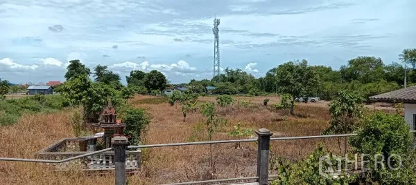 Land for sale in Bang Bo, Samut Prakan - Expansive land plot in Bang Bo with dry grass, trees, boundary fence and a telecom tower under a blue sky.
