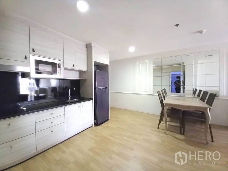 Condominium for rent in Khlong Toei, Bangkok - Modern kitchenette with black backsplash, microwave, refrigerator, and adjacent dining set.