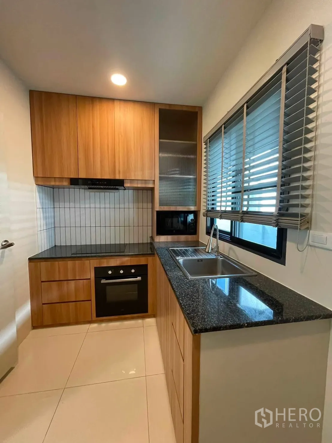 Detached House for rent in Bang Phli, Samut Prakan - Compact kitchen with granite countertops, wooden cabinetry, built-in oven, cooktop, sink, and window blinds.