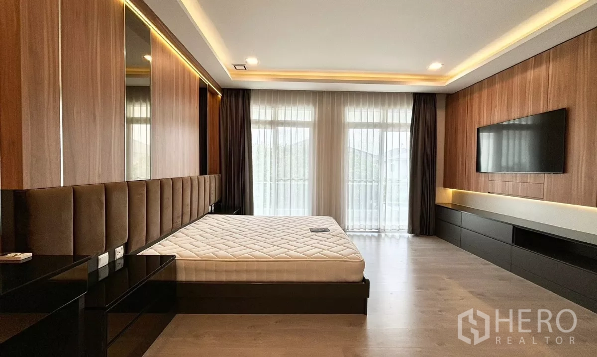 Detached House for rent or sale in Prawet, Bangkok - Spacious master bedroom with wood panel feature wall, TV cabinet and floor-to-ceiling windows.