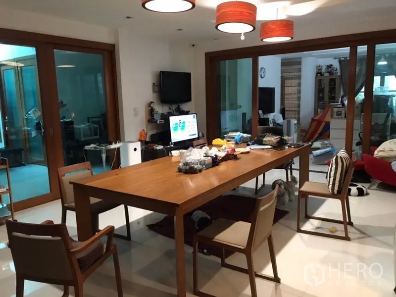 独立式住宅 出售在Lat Phrao, Bangkok - 餐厅配长木桌与吊灯，滑动玻璃门连接相邻起居空间。