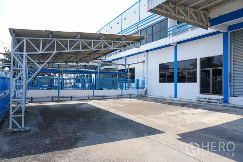 Factory for rent in Bang Sao Thong, Samut Prakan - Spacious concrete yard with metal canopies and blue perimeter fencing.