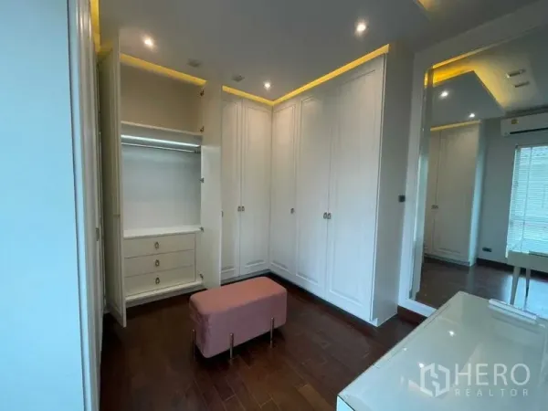 独立式住宅 出租或出售在Lat Krabang, Bangkok - 步入式衣帽间，白色通顶衣柜与大镜子，柔和灯光，粉色长凳。