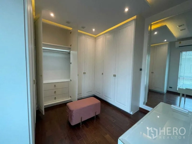 独立式住宅 出租或出售在Lat Krabang, Bangkok - 步入式衣帽间，白色通顶衣柜与大镜子，柔和灯光，粉色长凳。