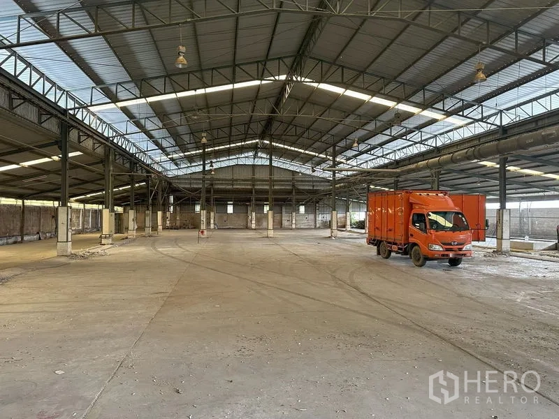 Factory for rent in Lat Lum Kaeo, Pathum Thani - Spacious factory interior with steel truss roof, skylight panels and an orange truck on the concrete floor.