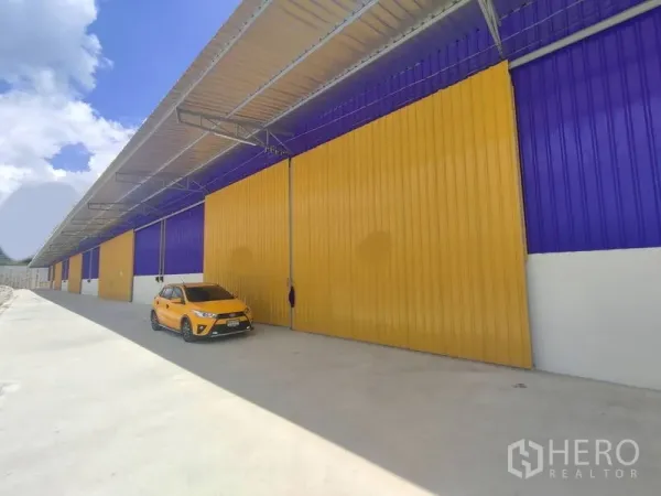 Warehouse for rent in Mueang Nonthaburi, Nonthaburi - Row of warehouse fronts with a covered drive and a parked vehicle along the concrete apron.