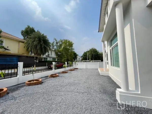 Detached House for sale in Lat Krabang, Bangkok - Spacious gravel front yard with white low wall, potted plants and the home’s front columns.