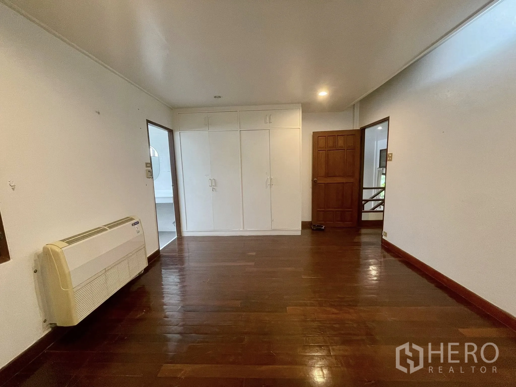 Detached House for rent in Pathum Wan, Bangkok - Bedroom with built-in wardrobe and wood floors connecting to a bathroom.