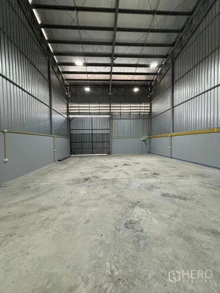 Warehouse for rent in Mueang Pathum Thani, Pathum Thani - Warehouse bay with concrete slab flooring and large loading door at the end.