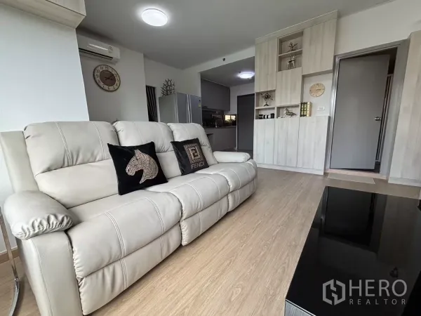 公寓 出租在Phra Khanong, Bangkok - 曼谷Bang Chak公寓客厅，奶油色皮沙发、嵌入式柜与木质地板，连通厨房。