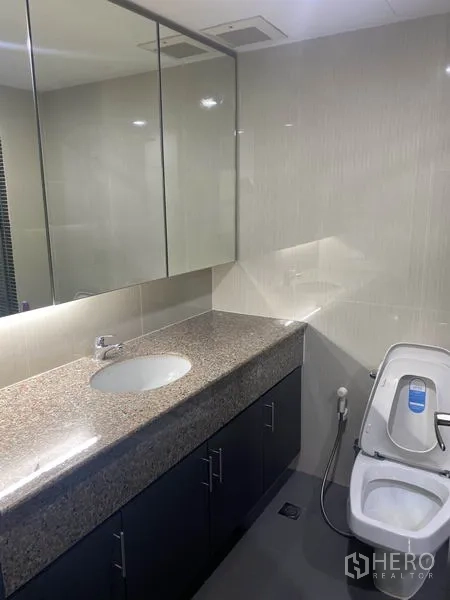 Condominium for rent in Khlong Toei, Bangkok - Modern bathroom with granite vanity, mirrored cabinets, and toilet.