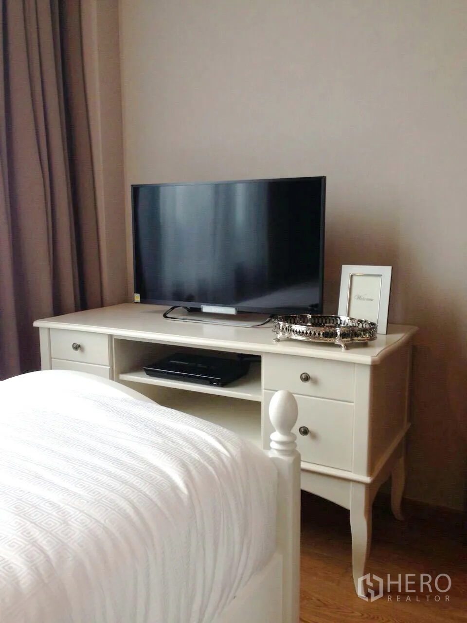 Condominium for rent in Khlong Toei, Bangkok - Bedroom media console with flat-screen TV on a white dresser and hardwood flooring.