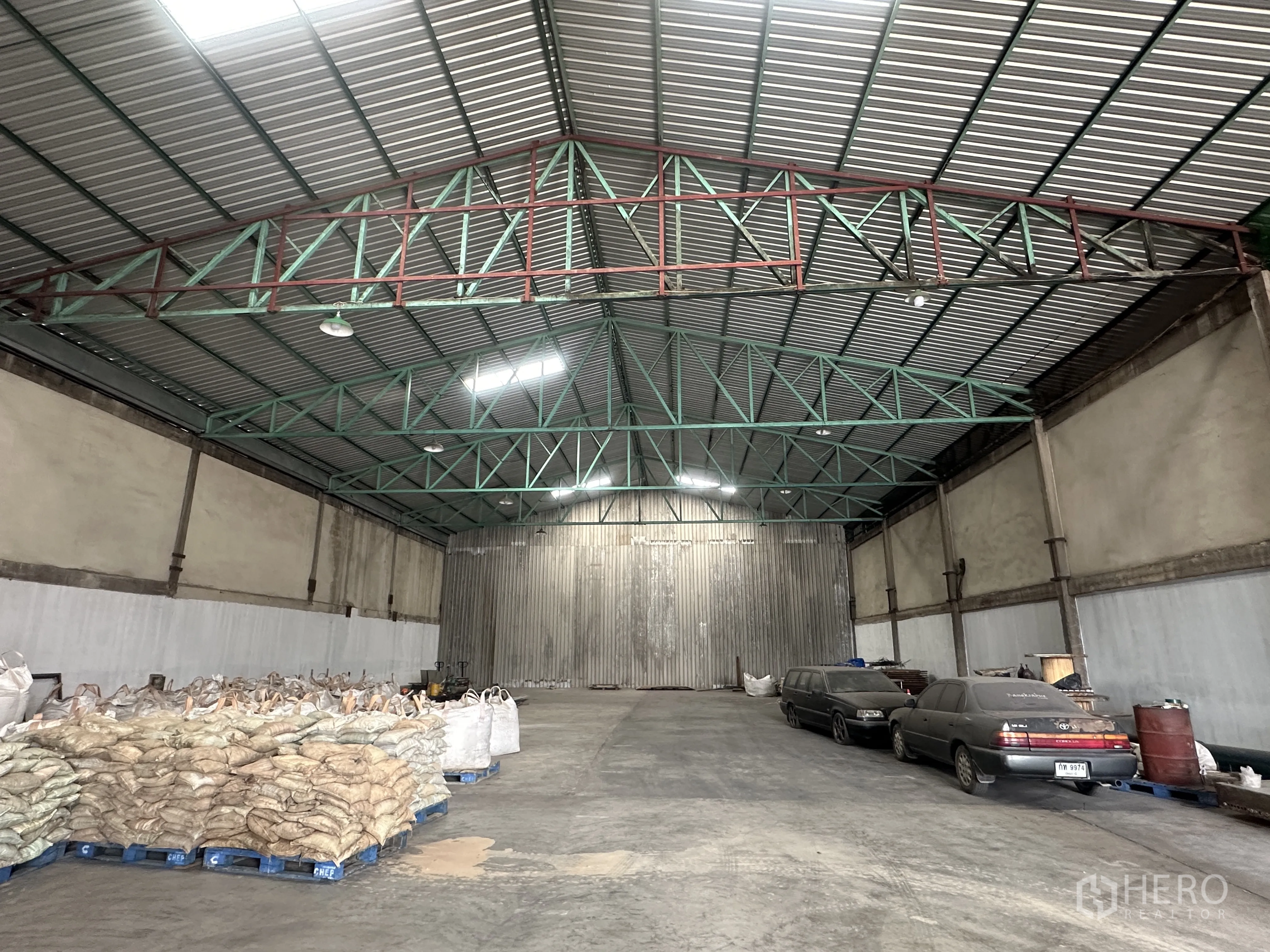 Warehouse for rent in Mueang Pathum Thani, Pathum Thani - Open-span storage hall showing reinforced concrete floor, steel roof beams and pallets along the walls.