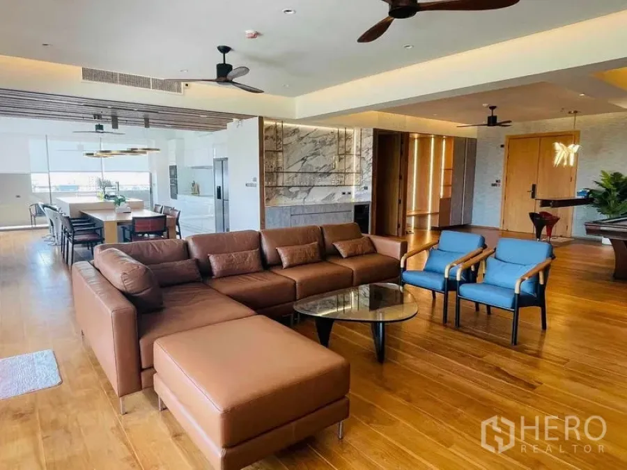 公寓 出租或出售在Watthana, Bangkok - 开放式起居与用餐区，皮沙发、蓝色单椅与大理石点缀墙。