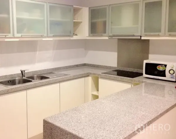 Condominium for rent in Khlong Toei, Bangkok - Bright U-shaped kitchen with granite countertops, breakfast bar, electric hob, microwave and frosted glass cabinets.