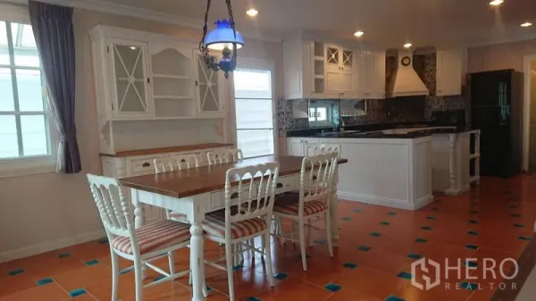 Detached House for rent in Mueang Samut Prakan, Samut Prakan - Dining area beside an open kitchen with white cabinetry, island, terracotta floor tiles and pendant light.