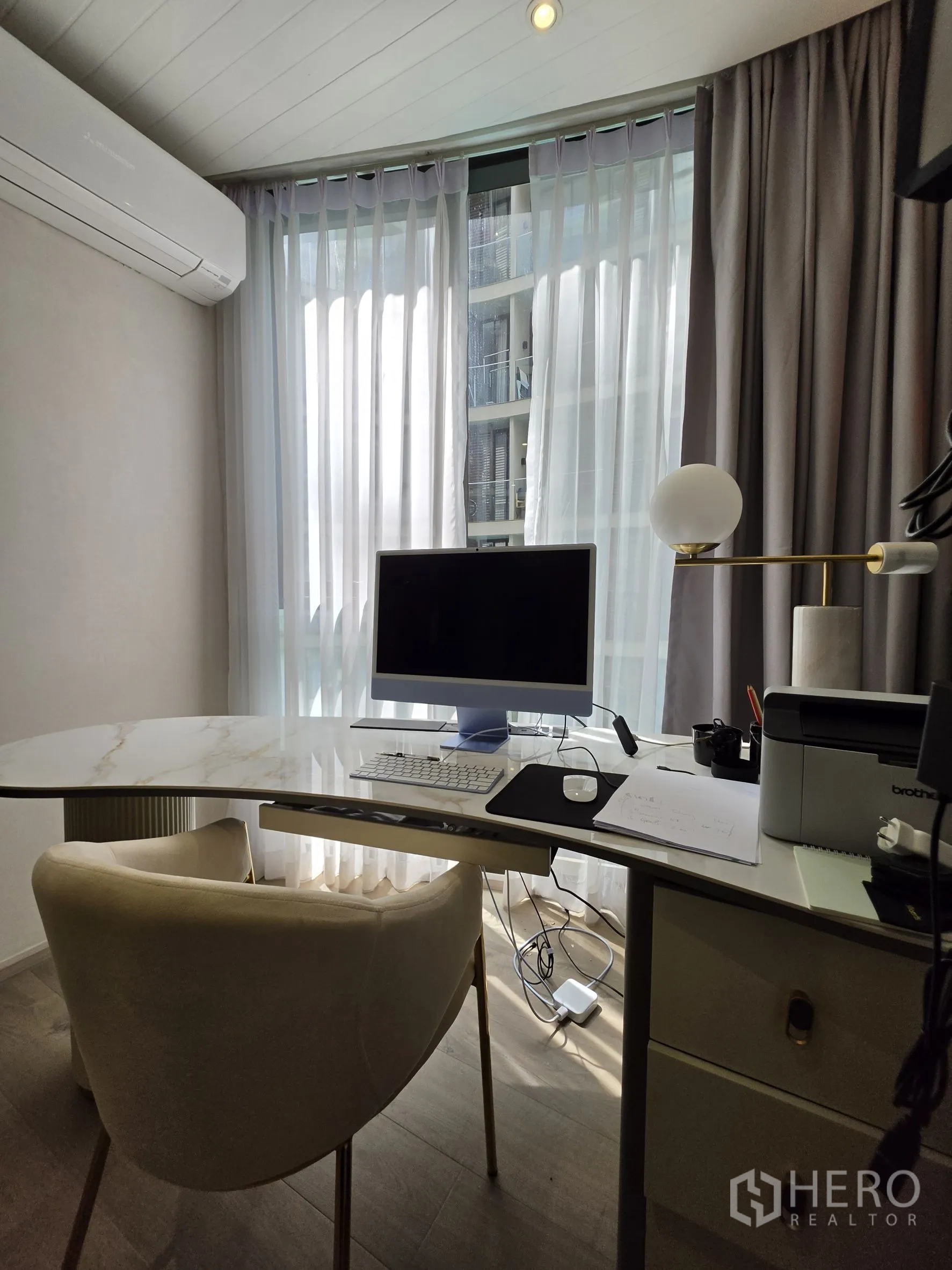 Condominium for rent in Khlong Toei, Bangkok - Curved marble-top desk and chair facing windows with sheer drapes.