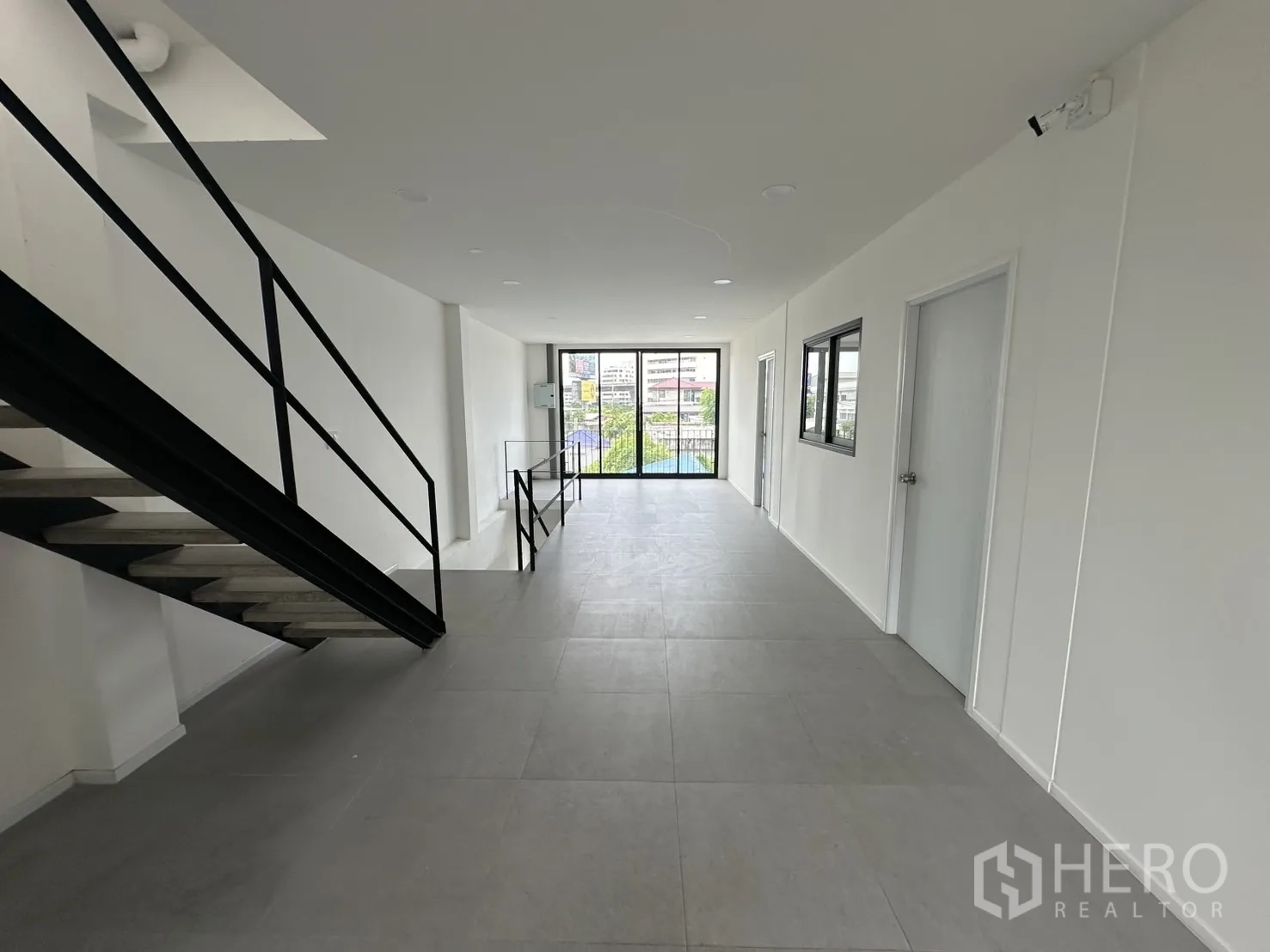 Home Office for rent or sale in Bang Na, Bangkok - Bright hallway with tiled floor and black handrails leading to balcony doors.
