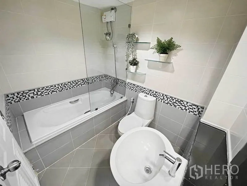 Condominium for rent in Khlong Toei, Bangkok - Bathroom with bathtub, overhead shower, vanity shelf and gray mosaic accents.