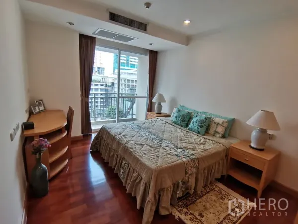 Condominium for rent in Khlong Toei, Bangkok - Cozy bedroom with a king bed, bedside tables, small desk, and sliding glass door to a city-view balcony.
