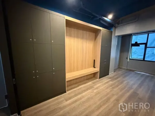 Home Office for rent in Watthana, Bangkok - Built-in storage cabinets and wood bench in an open workspace with window.
