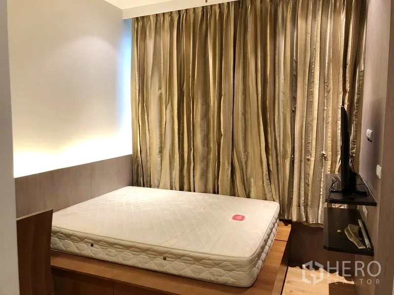 Condominium for rent in Khlong Toei, Bangkok - Cozy guest bedroom with platform bed, warm lighting, TV shelf, and heavy curtains.