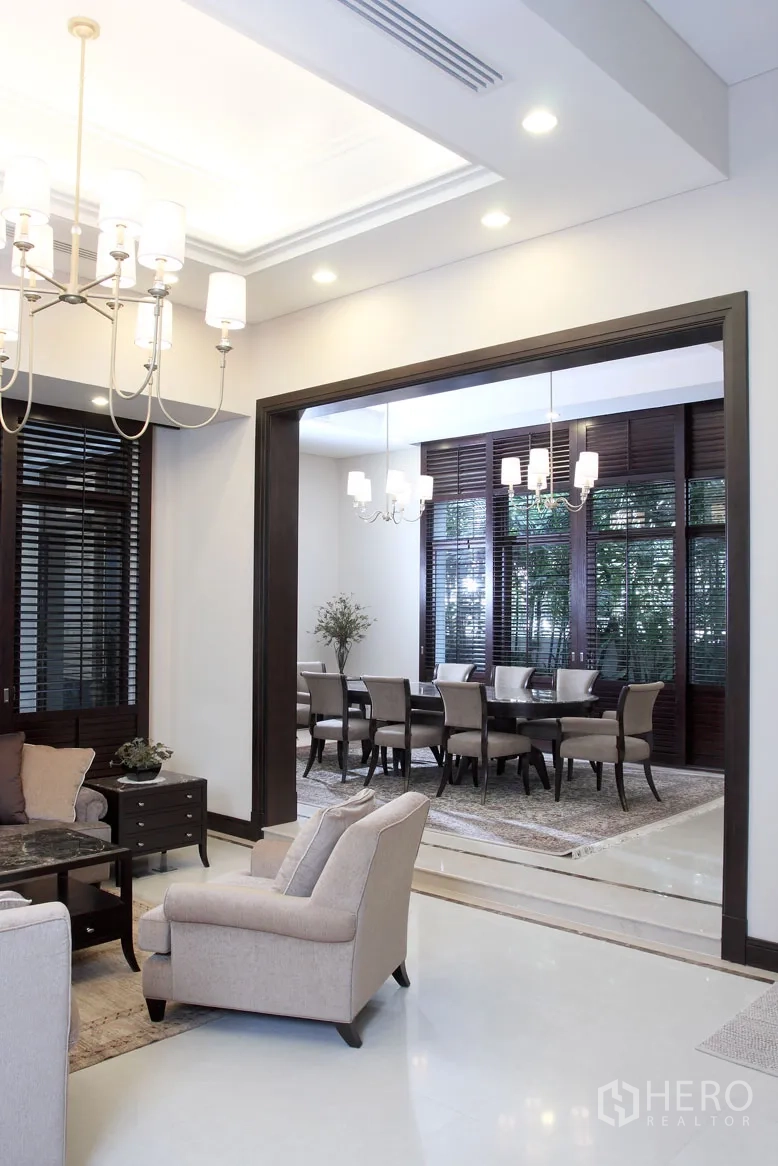 Detached House for rent in Khlong Toei, Bangkok - Bright living area opening to a formal dining room with chandeliers, dark wood trim and large window shutters.