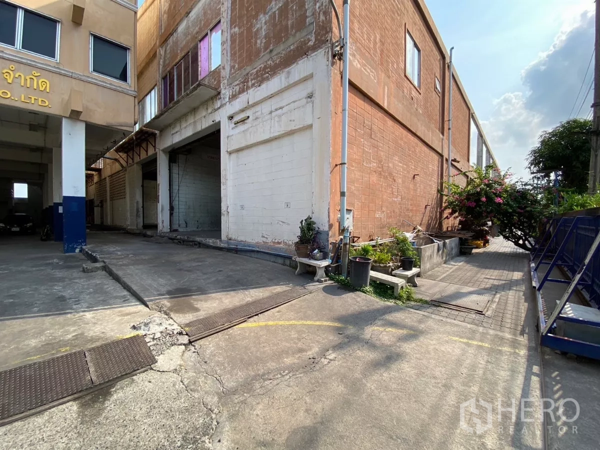 Factory for sale in Bang Phli, Samut Prakan - Loading bay area by brick factory wall with small planters near driveway.