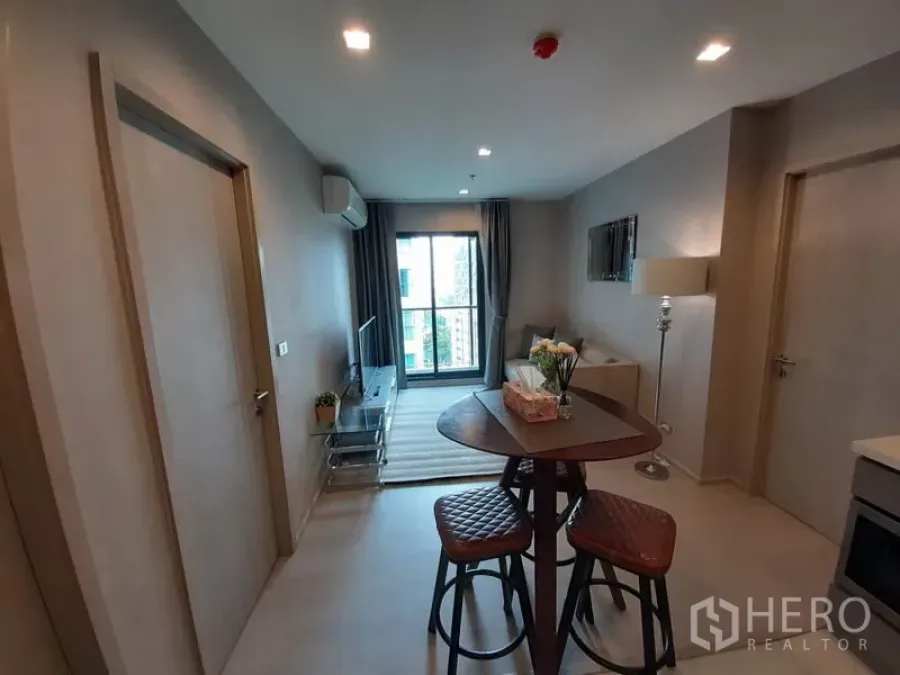 Condominium for rent or sale in Khlong Toei, Bangkok - Open-plan living and dining area with round table, sofa, TV console and balcony window.