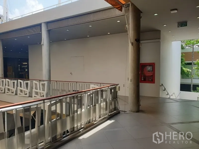 零售空间 出租在Khlong Toei, Bangkok - 现代购物中心二层走廊，金属栏杆、楼梯与消防箱，采光充足。
