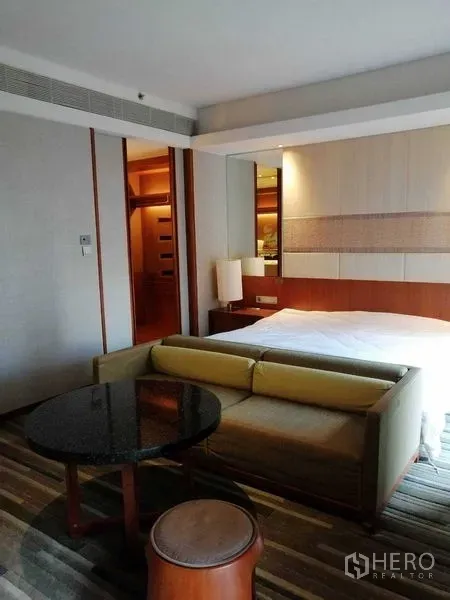 Condominium for rent in Pathum Wan, Bangkok - Bedroom overview with bed, small sofa, round coffee table and bedside lamps.