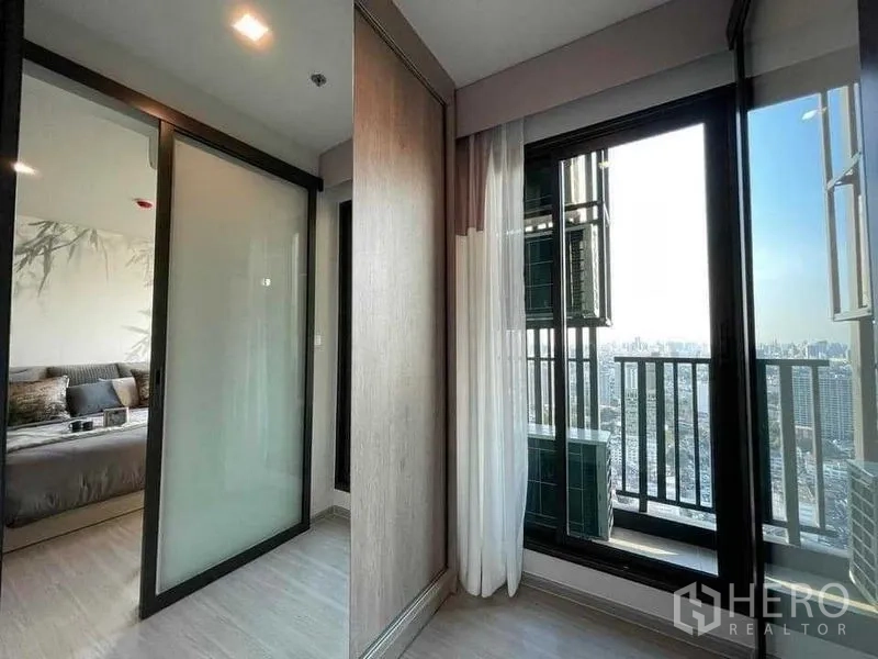 Condominium for rent in Chatuchak, Bangkok - Hallway to the balcony with sliding glass doors and expansive city views from a high-rise.