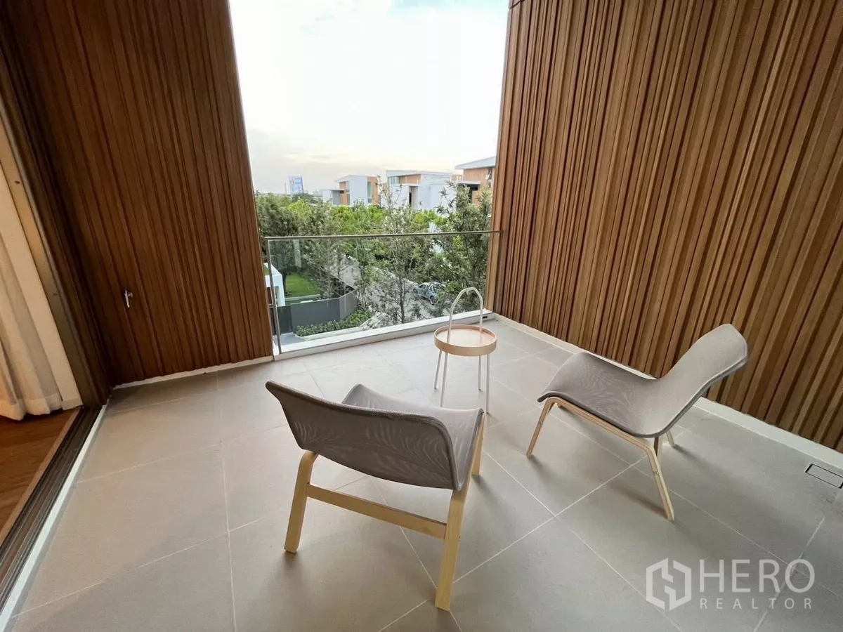 Detached House for rent in Saphan Sung, Bangkok - Covered balcony with two lounge chairs, glass balustrade and wood slat walls overlooking greenery.