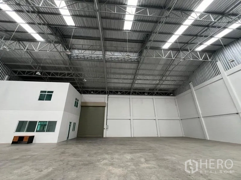 Factory for rent in Phra Samut Chedi, Samut Prakan - High-clearance production hall with steel truss roof, skylights, concrete floor and wide loading shutter.