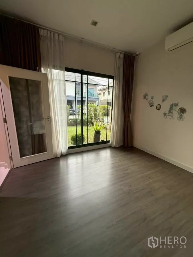 Detached House for rent or sale in Bang Phli, Samut Prakan - Ground‑floor room opening to a small garden through sliding glass doors and sheer curtains.