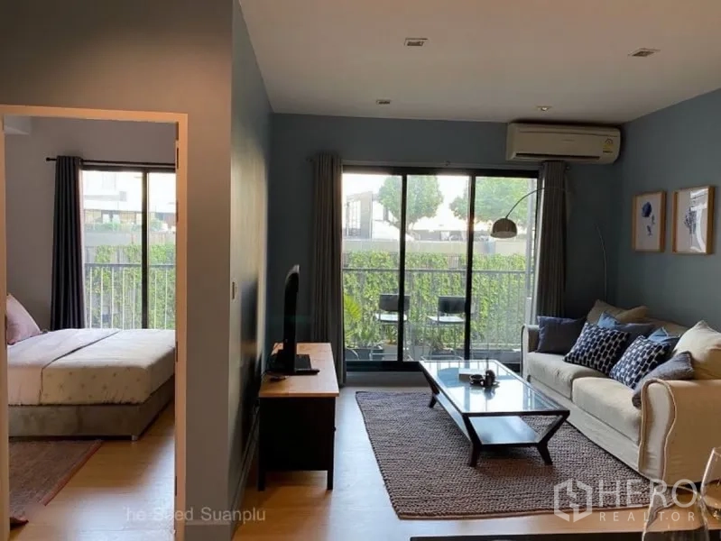 Condominium for rent or sale in Sathon, Bangkok - Bright living room with sliding glass to a greenery-facing balcony and the bedroom nearby.