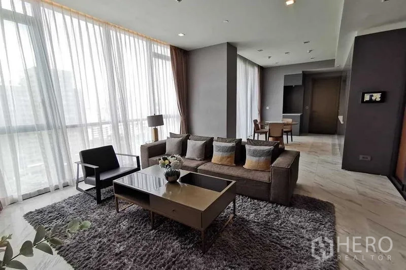 Condominium for rent or sale in Watthana, Bangkok - Living area with L-shaped sofa, shaggy rug and full-height curtains.