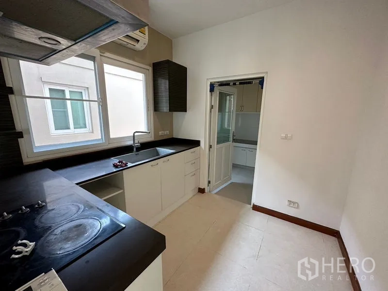 独立式住宅 出租或出售在Pak Kret, Nonthaburi - 西式厨房，黑色台面与窗户，连接泰式厨房。