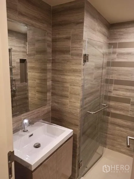 Condominium for sale in Din Daeng, Bangkok - Modern bathroom featuring a vanity and a glass-enclosed shower with wood-tone tiles.