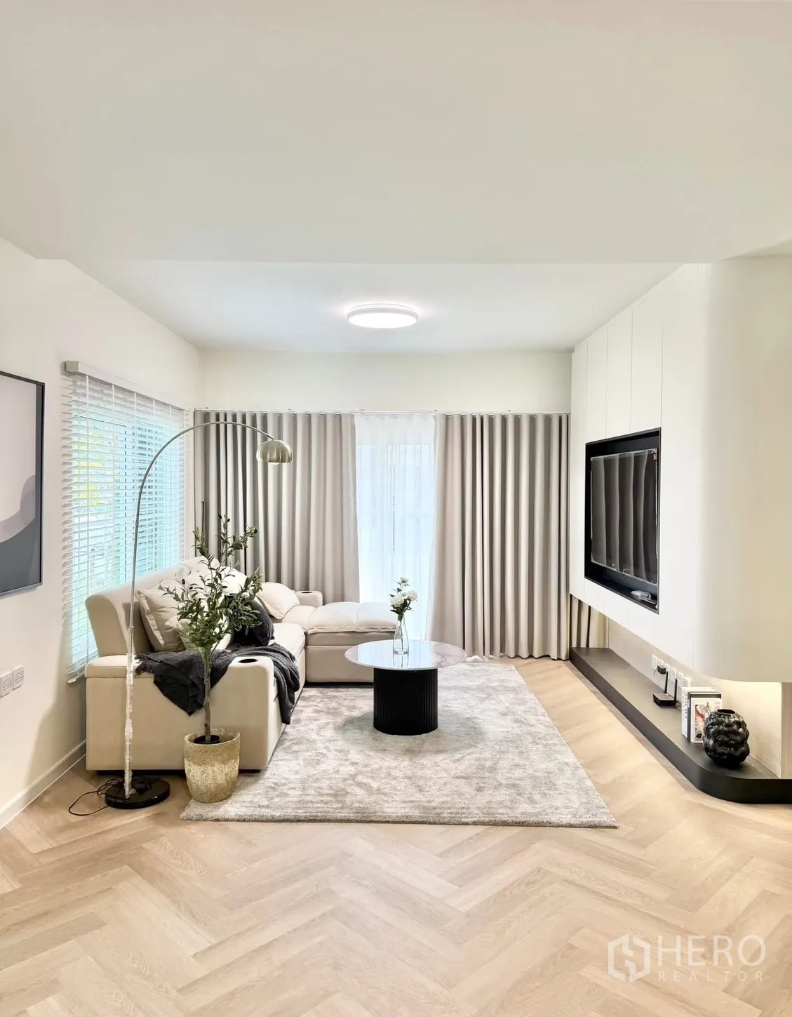 Detached House for rent in Bang Phli, Samut Prakan - Contemporary living room with L-shaped sofa, rug, TV wall and herringbone wood floors.