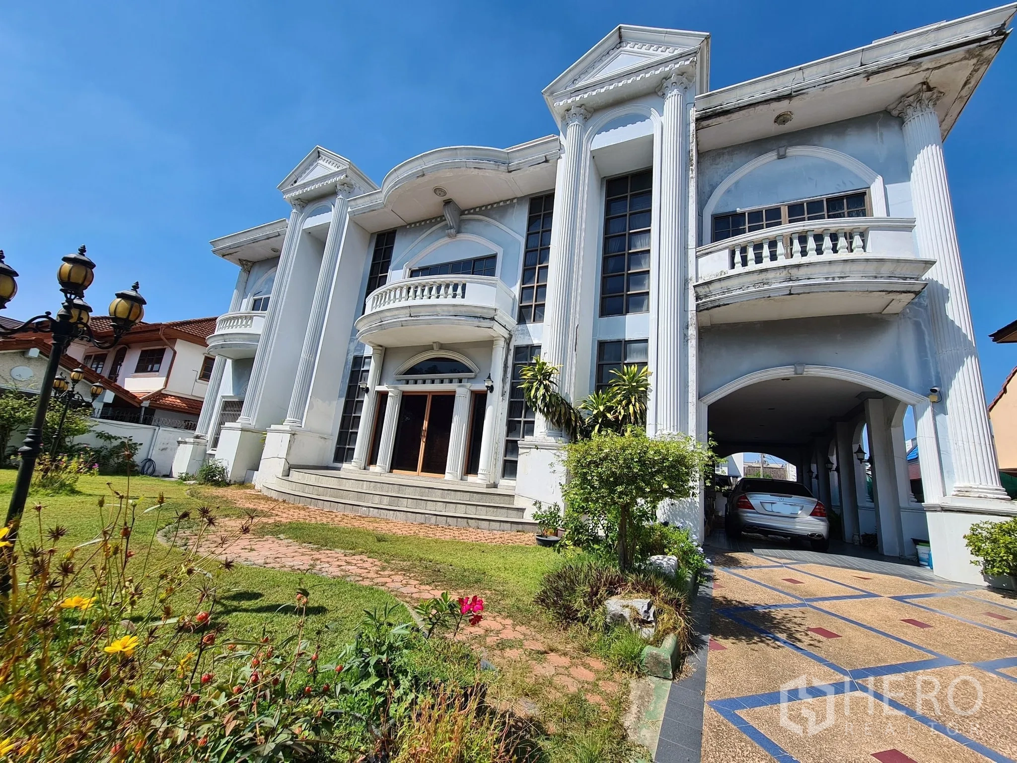 Detached House for sale in Chatuchak, Bangkok - Angle view of the mansion with tall columns, lawned garden and covered driveway.