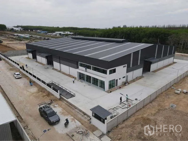 货栈 出租或出售在Nikhom Phatthana, Rayong - 航拍图：带前置办公楼、围墙及大型卡车回转场的现代仓库园区。