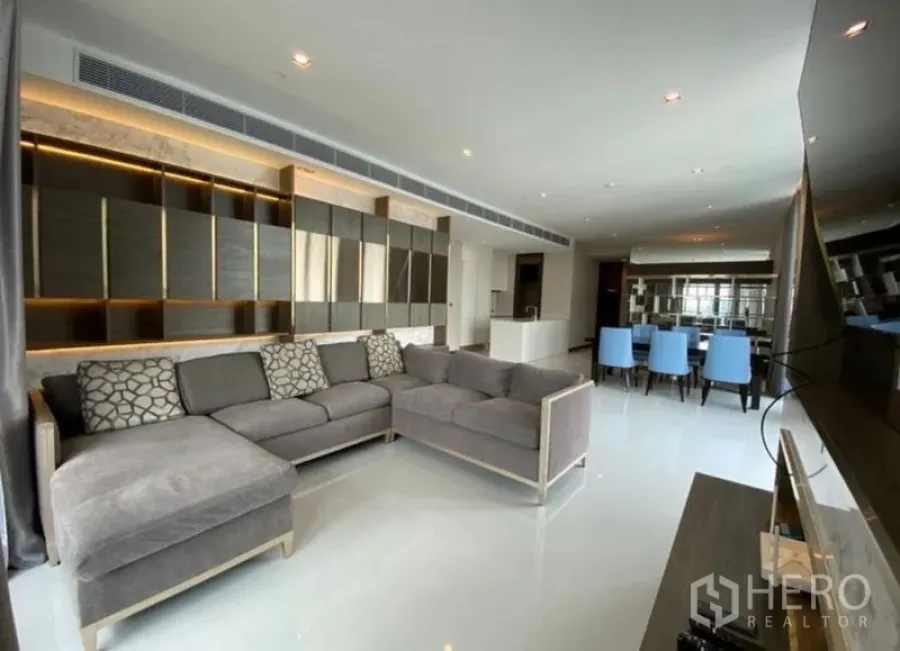 Condominium for rent in Khlong Toei, Bangkok - Open-plan living and dining room with L-shaped sofa, blue dining chairs and a modern panel wall.