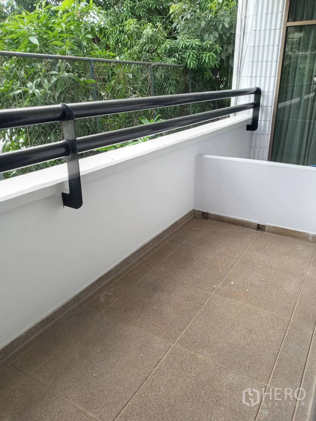 房间 出租在Watthana, Bangkok - 私家阳台，瓷砖地面与黑色栏杆，面向绿树景观。