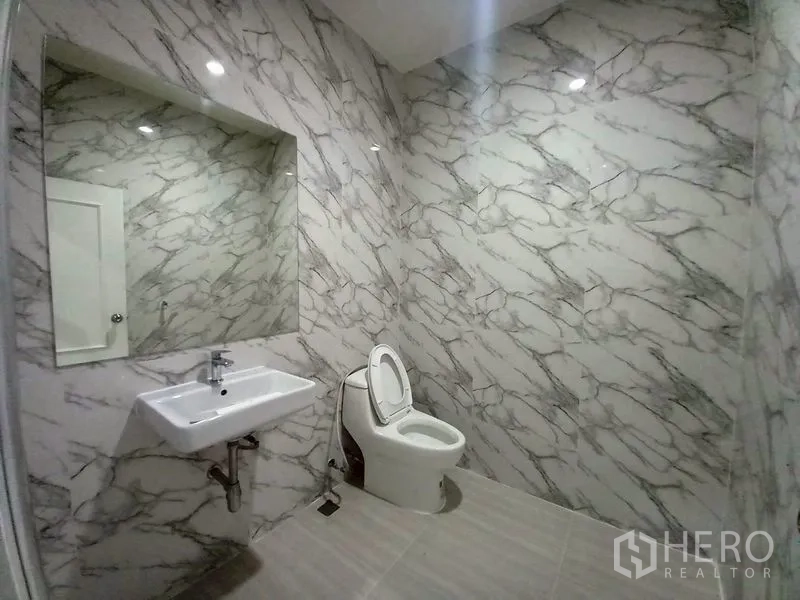 Condominium for rent in Watthana, Bangkok - Bathroom with marble-pattern walls, large mirror, basin and toilet.