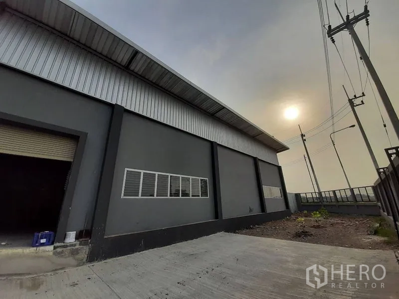 Factory for rent in Lam Luk Ka, Pathum Thani - Side elevation of the factory with long windows and driveway under evening sun.