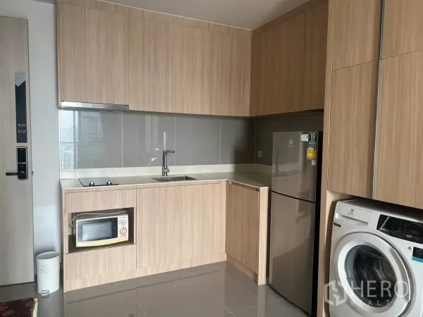 Condominium for rent or sale in Chatuchak, Bangkok - Modern U‑shaped kitchen with light wood cabinetry, sink, cooktop, microwave, fridge and washing machine.