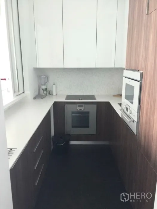 Condominium for rent or sale in Pathum Wan, Bangkok - Compact U-shaped kitchen with white countertops and built-in oven